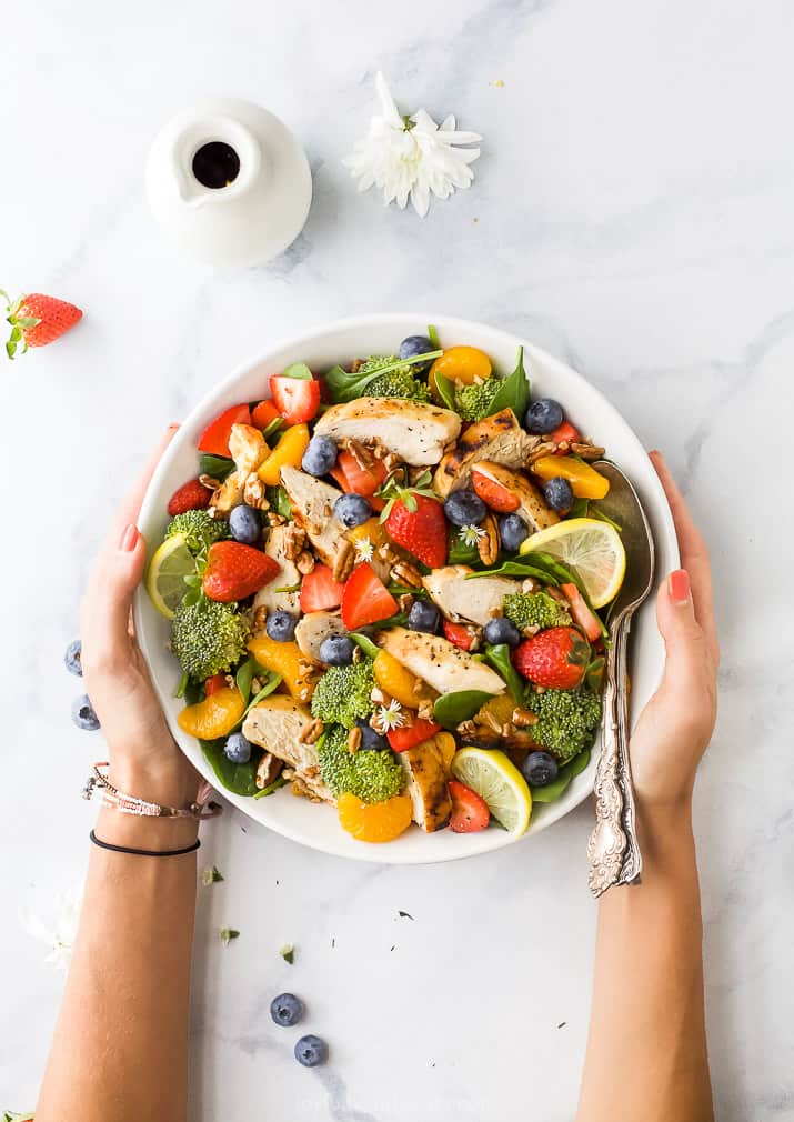 detox strawberry chicken salad with honey mustard dressing with hands around a bowl