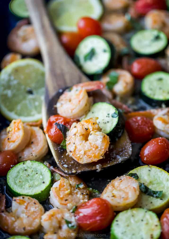a wooden spoon scooping Easy Garlic Parmesan Sheet Pan Shrimp and Zucchini on a pan