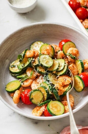 Bowl of sheet pan shrimp with fresh basil as a garnish.