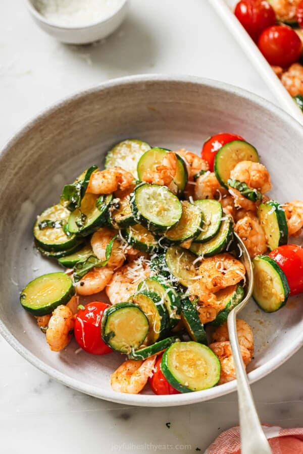 Bowl of sheet pan shrimp with fresh basil as a garnish.