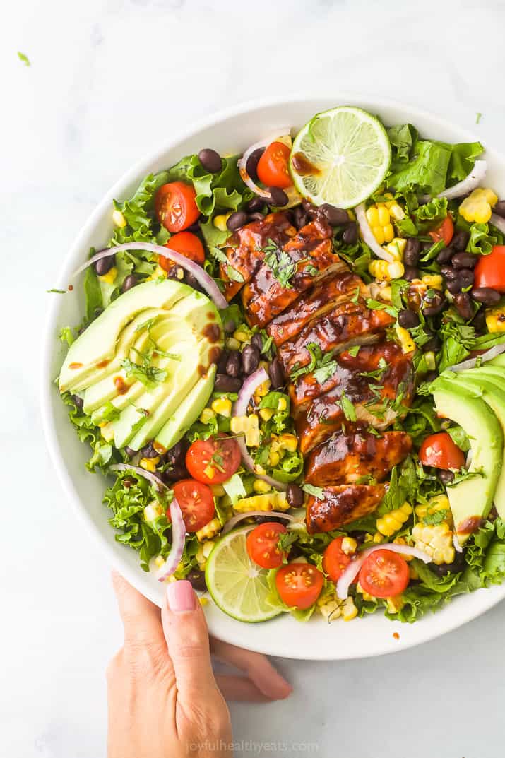a large salad with sliced BBQ chicken, avocado, and lime slices
