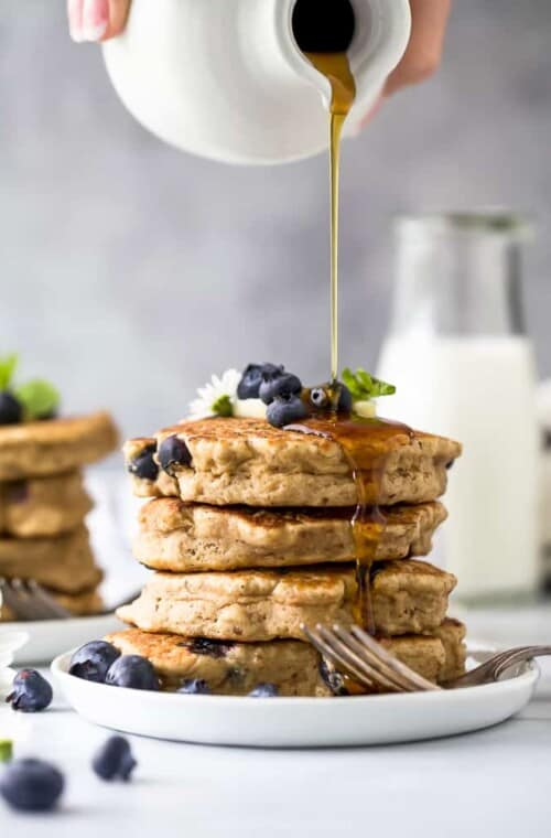 stack of healthy vegan blueberry pancakes with syrup being poured over them