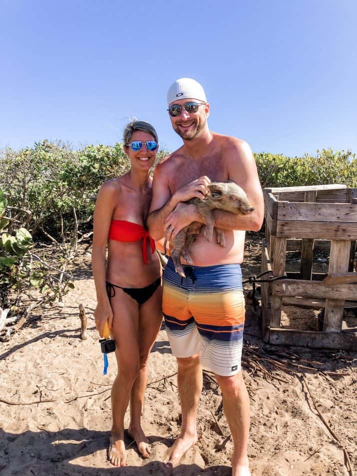 picture of a guy and girl holding a baby swimming pig on bahamas island