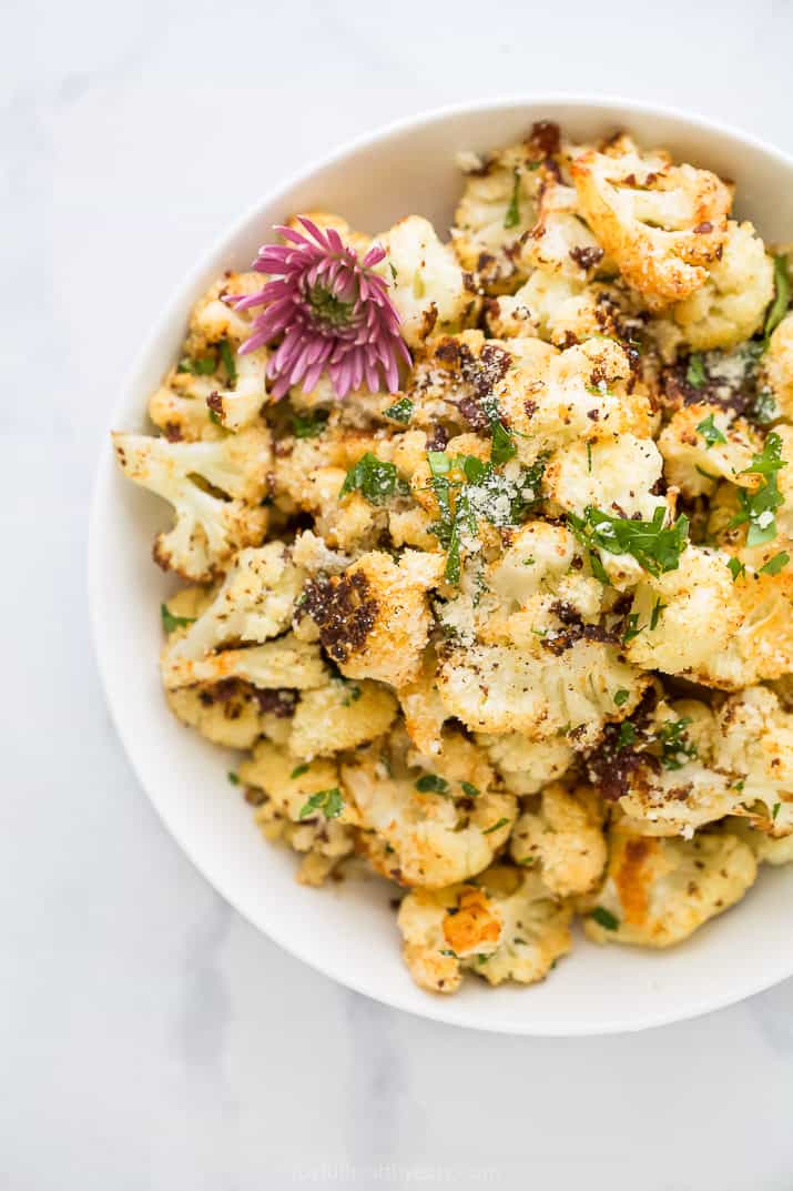 overhead photo of low carb parmesan roasted caulilfower in a bowl with flowers