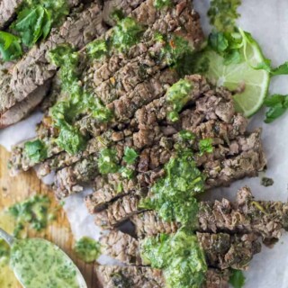 the best marinated grilled flank steak on a cutting board with chimichurri sauce