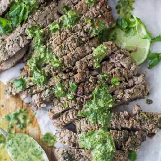 the best marinated grilled flank steak on a cutting board with chimichurri sauce