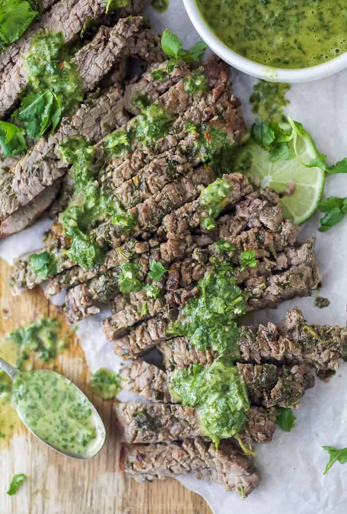 the best marinated grilled flank steak on a cutting board with chimichurri sauce