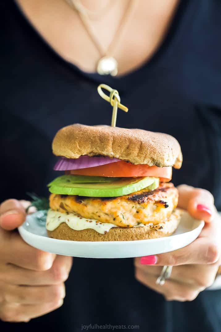 a person holding a grilled salmon burger with lemon garlic aioli on a plate