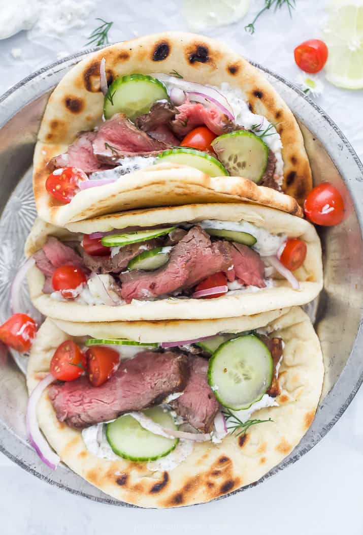 overhead photo of easy grilled steak gyros with tzatziki sauce and vegetables in a serving dish