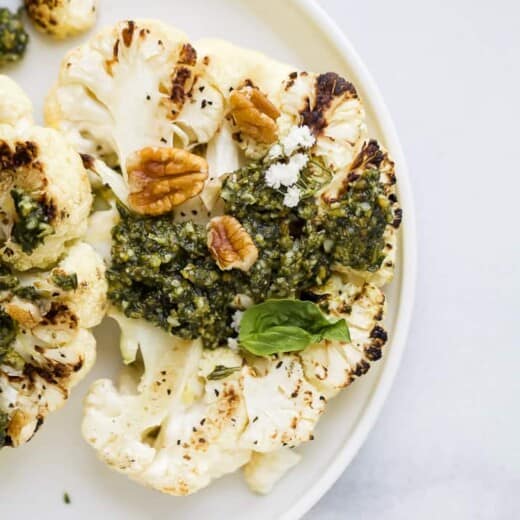 grilled cauliflower steaks with basil pecan pesto on a plate