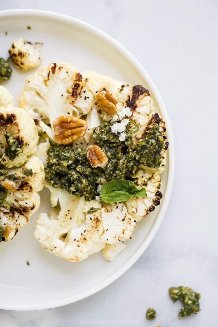 grilled cauliflower steaks with basil pecan pesto on a plate