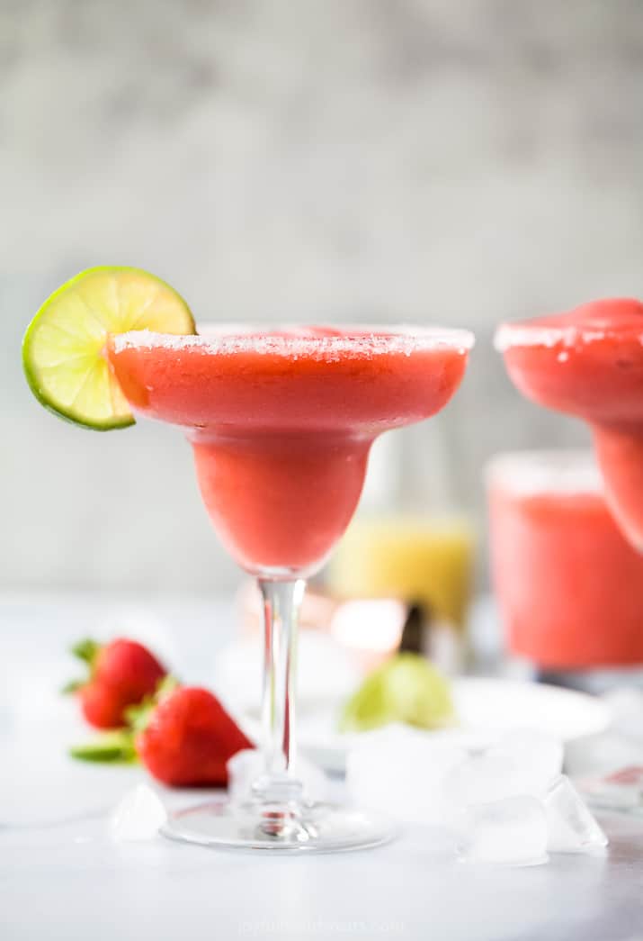 side photo of the ultimate frozen strawberry margaritas in a glass with a lime on the rim