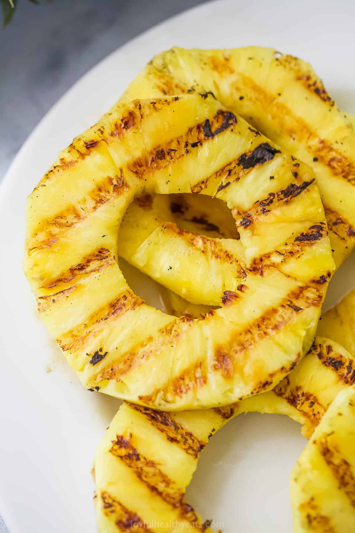 Juicy Grilled Pineapple is the easiest summer dessert and also the tastiest! Serve it as-is or fancy it up with a scoop of ice cream. Closeup of grilled pineapple rings on plate