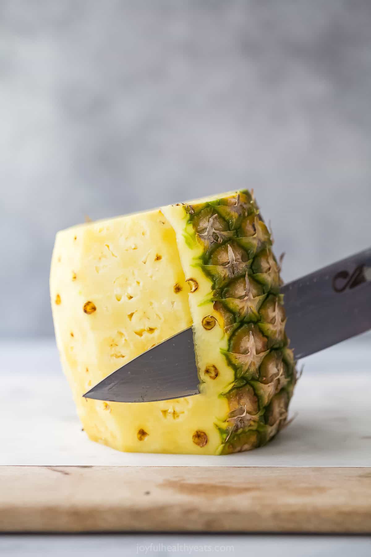 Knife slicing rind off of pineapple