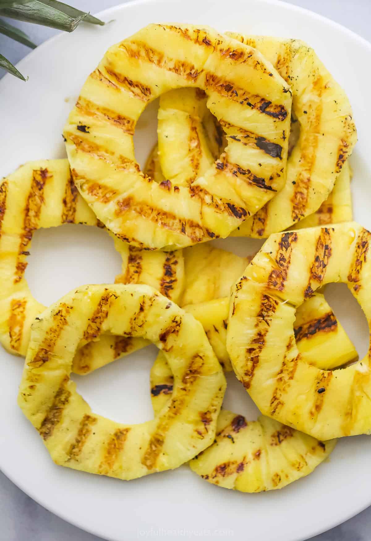 Juicy Grilled Pineapple is the easiest summer dessert and also the tastiest! Serve it as-is or fancy it up with a scoop of ice cream. Overhead view of grilled pineapple slices on plate
