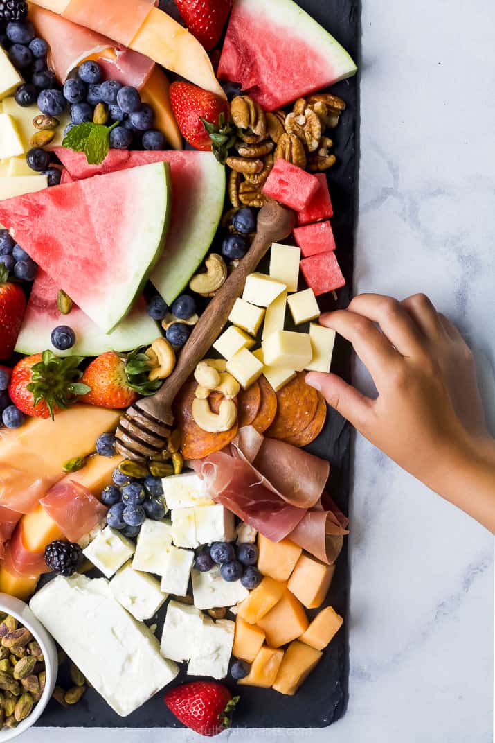 overhead photo of summer cheese board with hand grabbing food