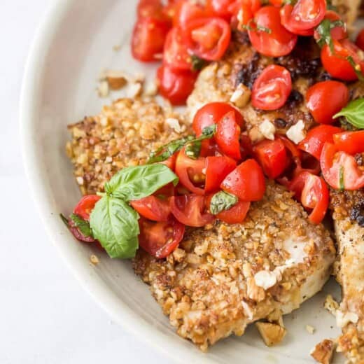 a bunch of pecan crusted tilapia with tomato bruschetta on a plate with fresh basil