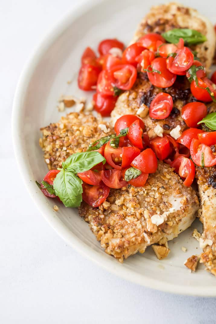 a bunch of pecan crusted tilapia with tomato bruschetta on a plate with fresh basil