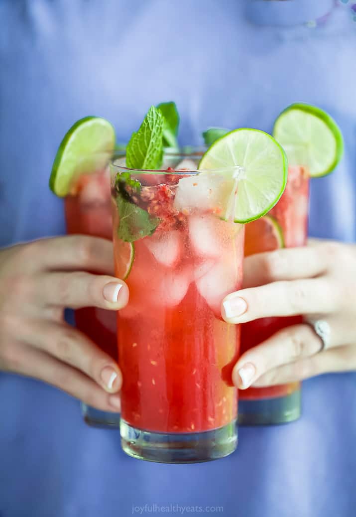 hands holding three glasses filled with the best fresh raspberry mojito recipe