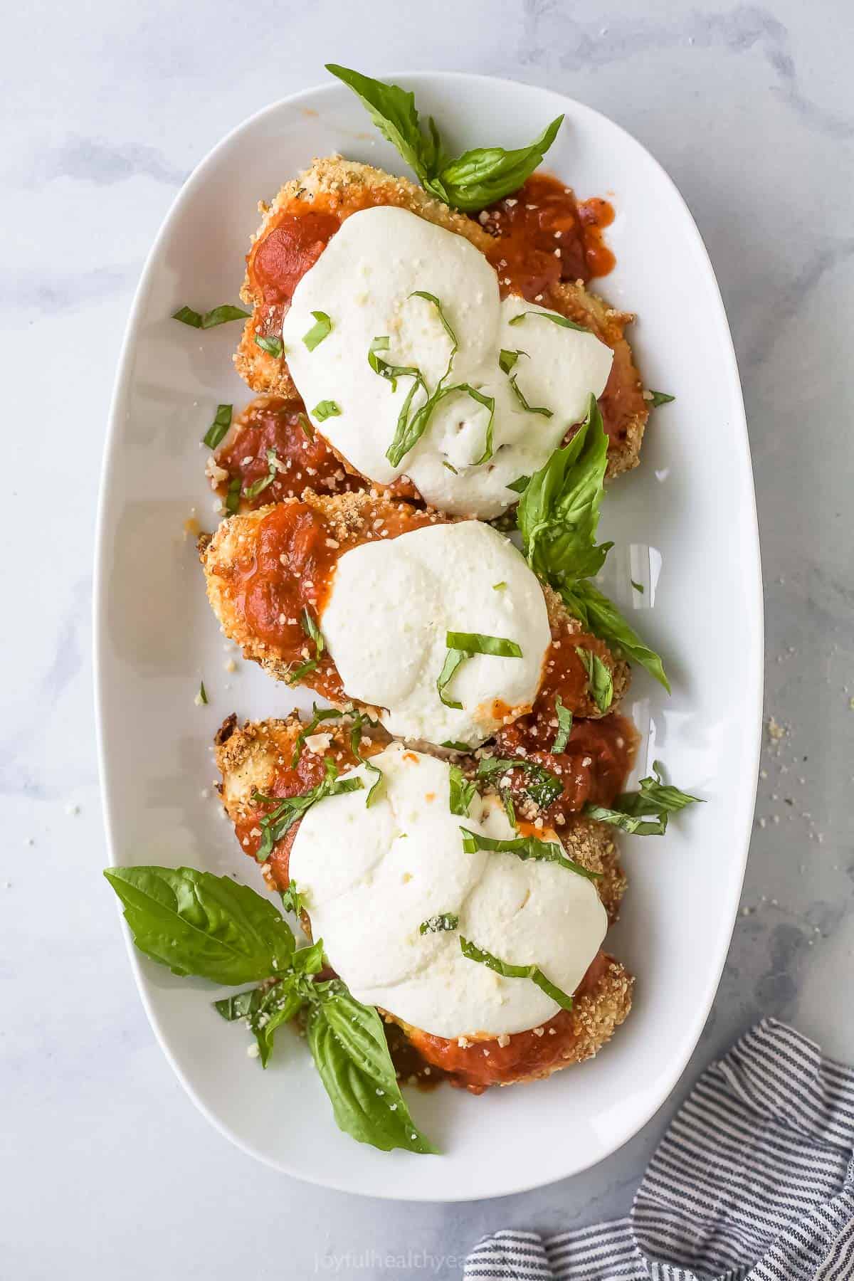 Three pieces of baked chicken parmesan on a plate. 