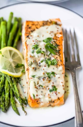 close up photo of pan seared salmon drizzled with creamy dijon sauce on a plate with asparagus
