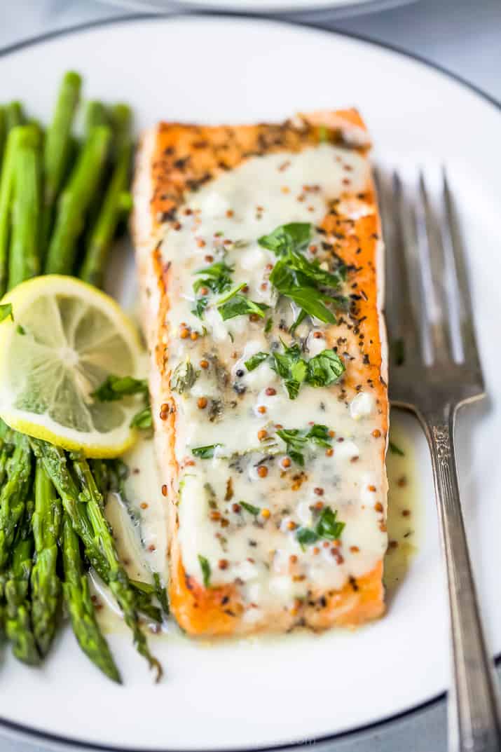 close up p،to of pan seared salmon drizzled with creamy dijon sauce on a plate with asparagus