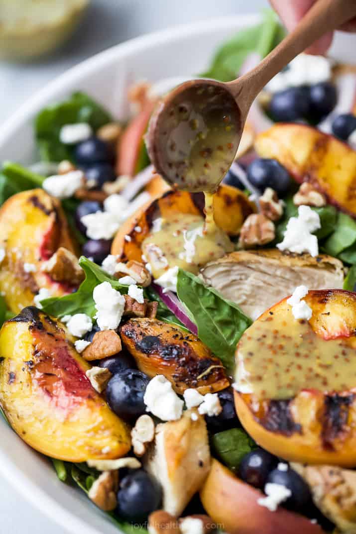 dressing being poured over grilled peach chicken salad