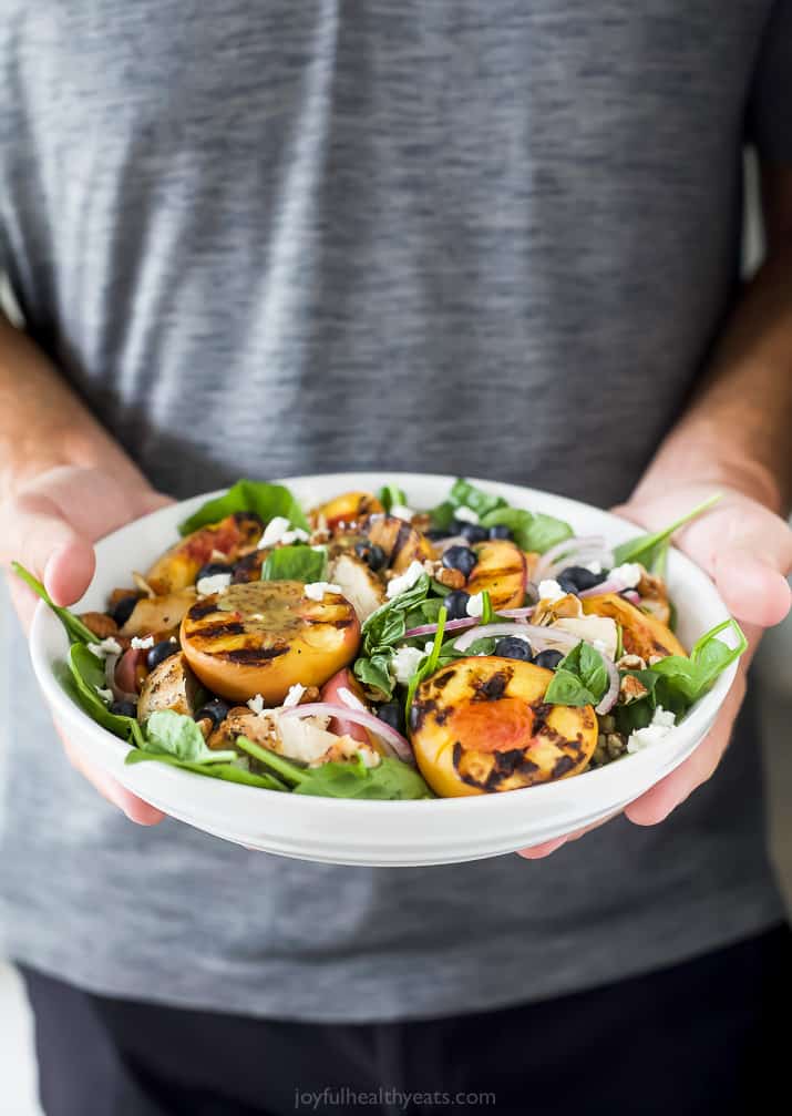 a man holding a bowl filled with grilled peach chicken salad