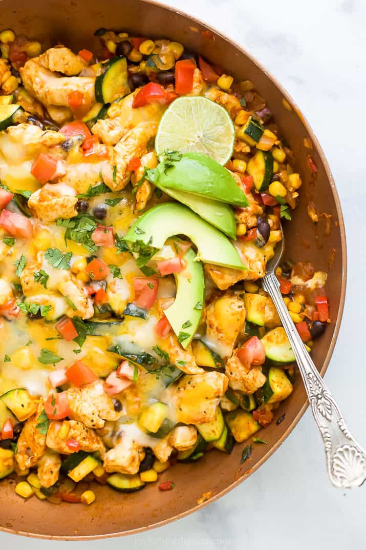 Overhead view of a chicken enchilada skillet topped with melted cheese, avocado slices, and lime.