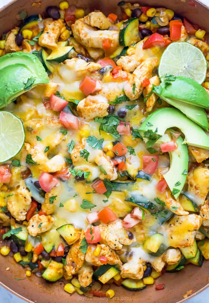 Overhead view of a chicken enchilada skillet topped with melted cheese, avocado slices, and lime.