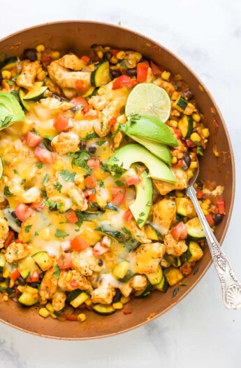 Overhead view of a chicken enchilada skillet topped with melted cheese, avocado slices, and lime.