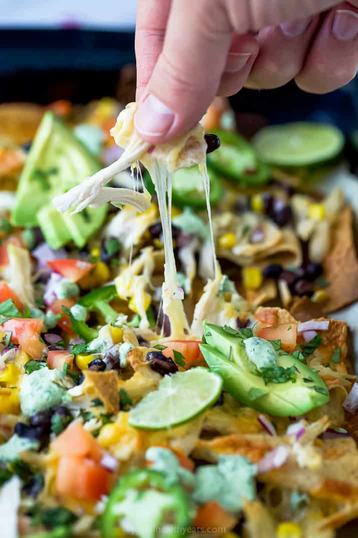 a hand pulling torilla chips from a pan of sheet pan chicken nachos