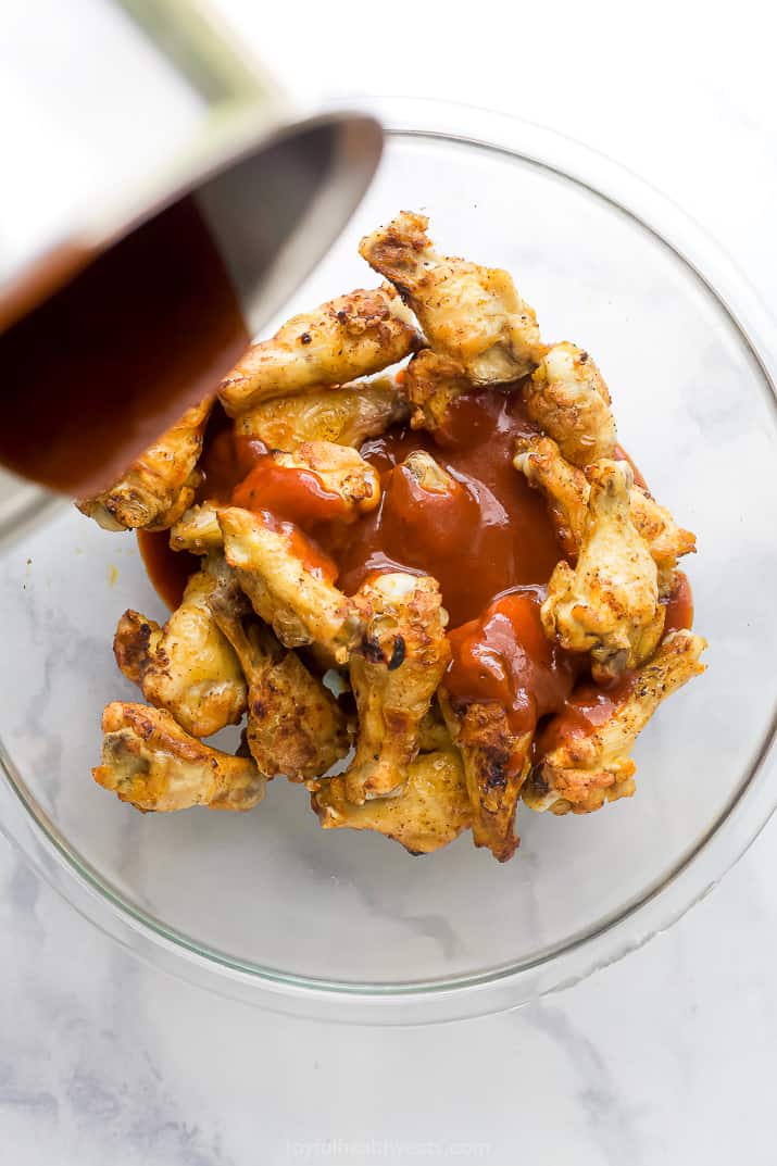 sweet and spicy bbq sauce being poured over baked chicken wings