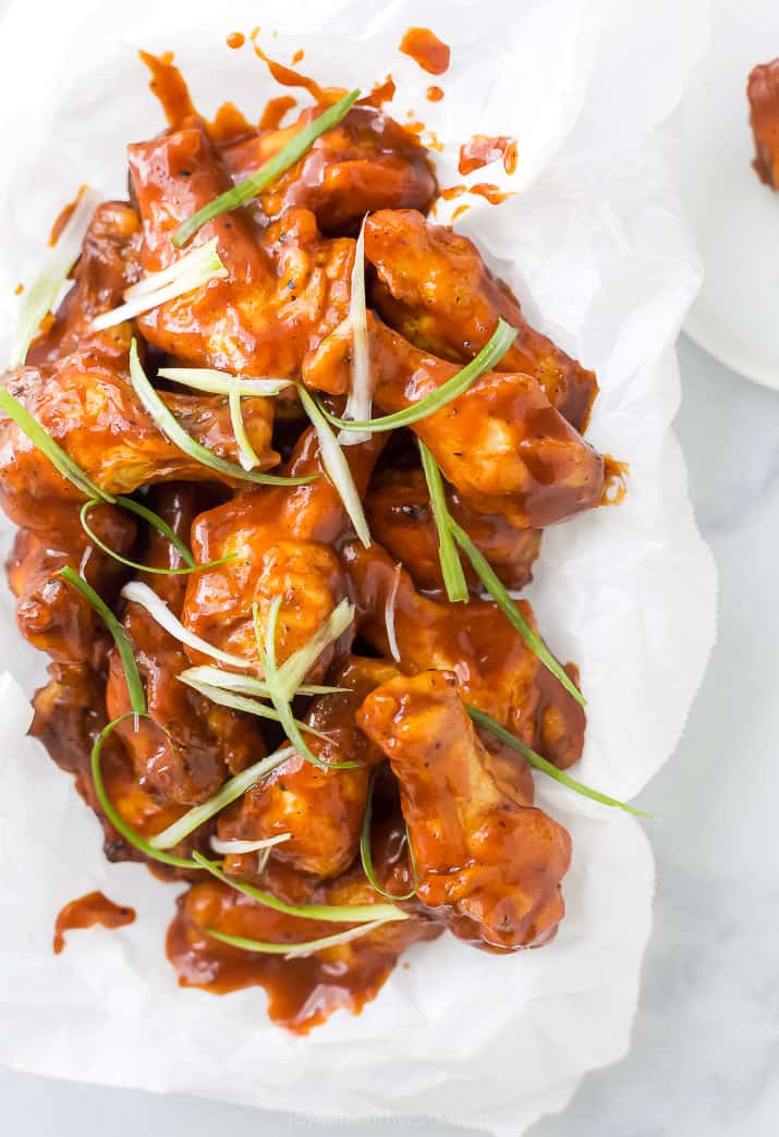 close up photo of baked sweet and spicy bbq chicken wings in a basket with green onions