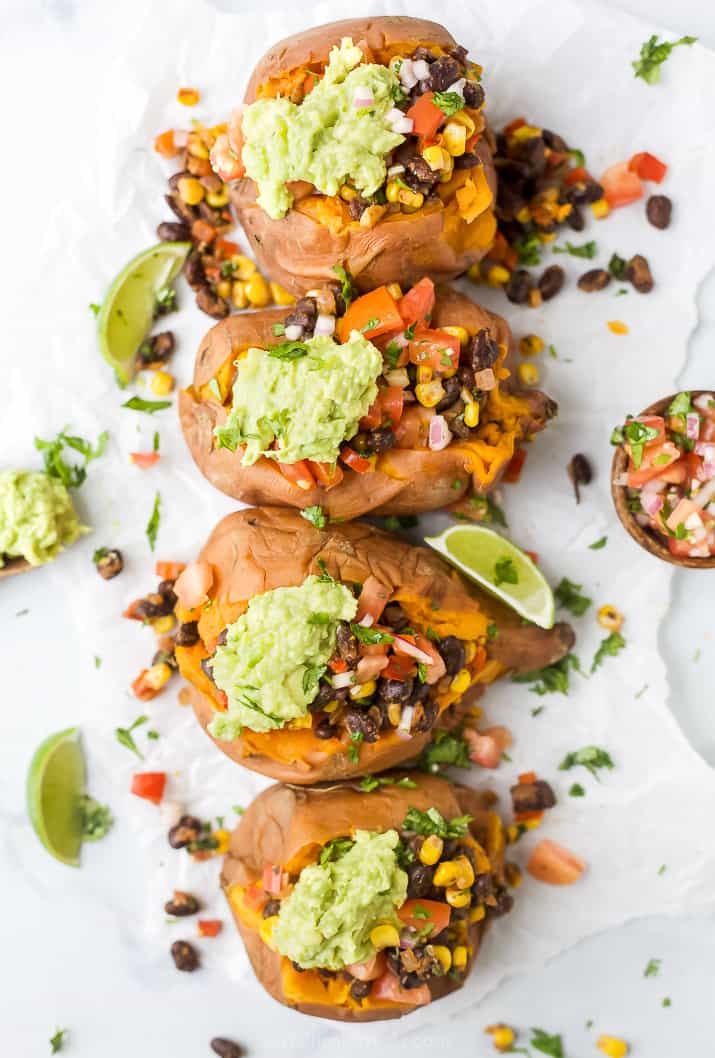overhead photo of four easy vegan black bean stuffed sweet potatoes with guacamole on top