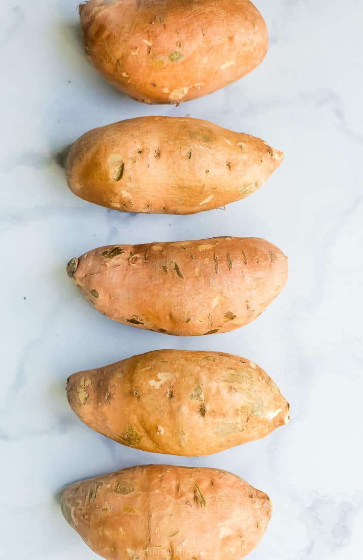 Raw sweet potatoes lined up on a board.