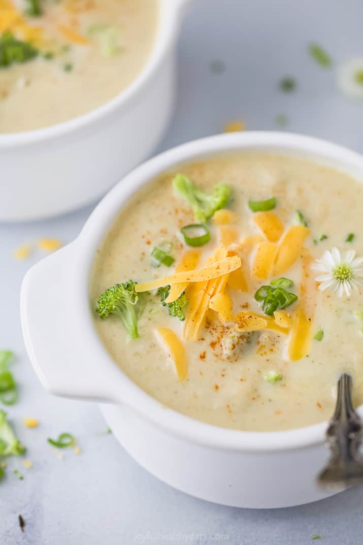 closeup side photo of easy crockpot broccoli cheese soup topped with cheese and green onions