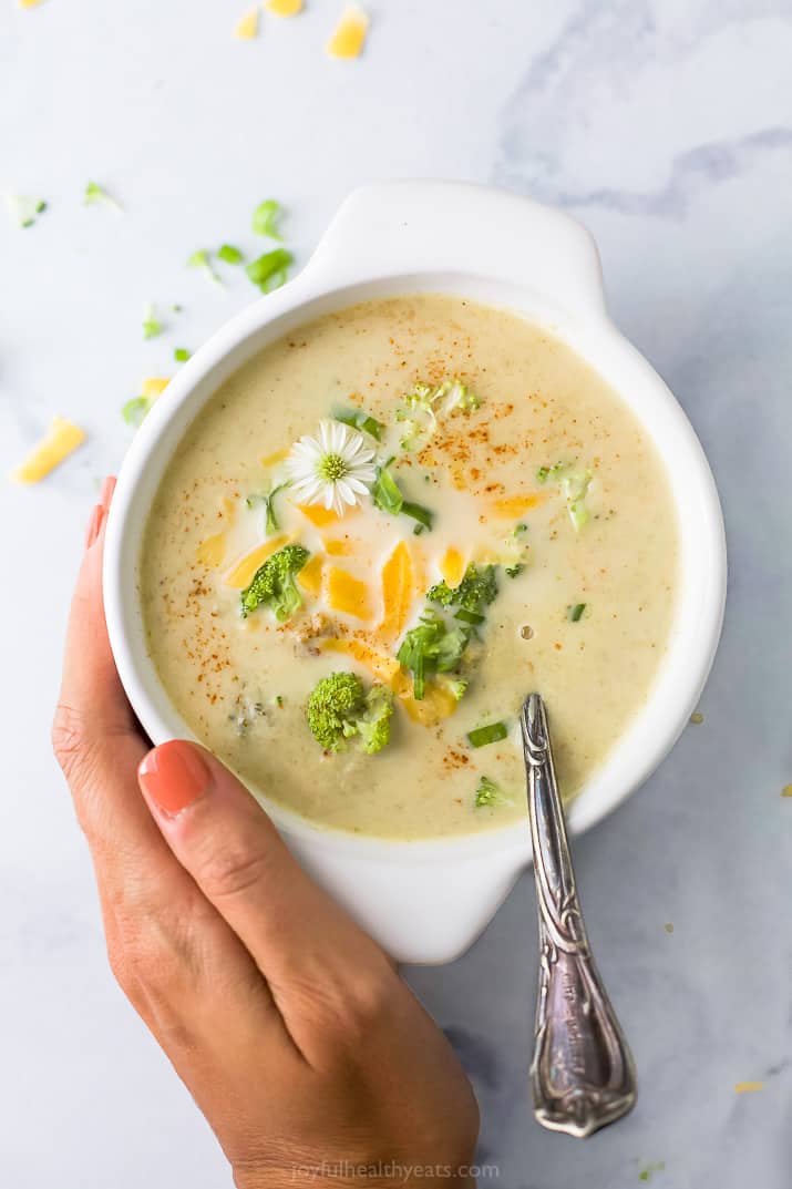 a hand holding a bowl of easy crockpot broccoli cheese soup