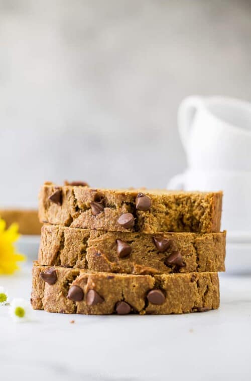 A stack of three pieces of pumpkin banana bread on a counter with two mugs in the background