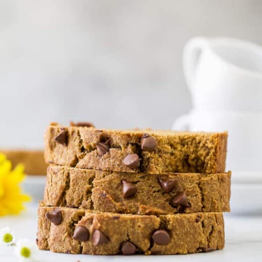 A stack of three pieces of pumpkin banana bread on a counter with two mugs in the background