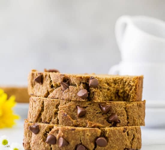 A stack of three pieces of pumpkin banana bread on a counter with two mugs in the background