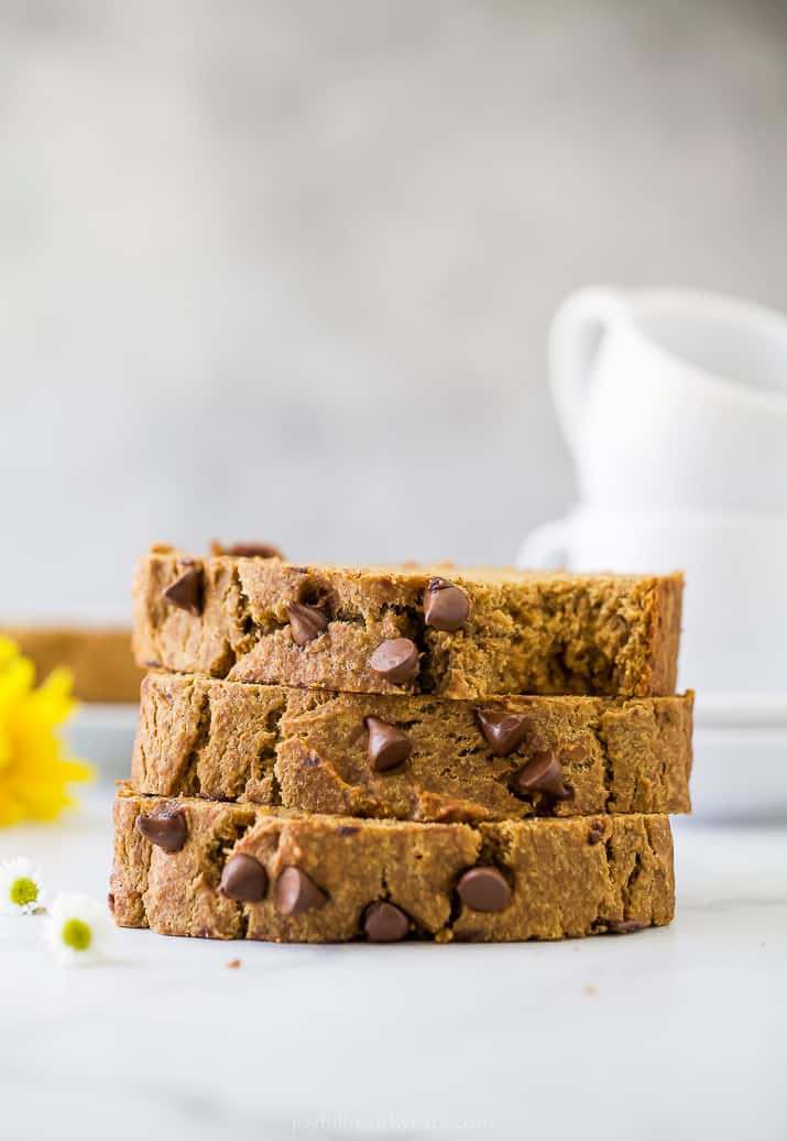 A stack of three pieces of pumpkin banana bread on a counter with two mugs in the background