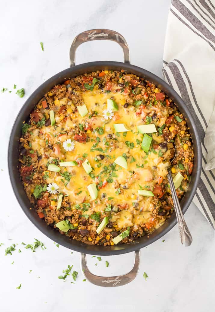 healthy one pan cheesy quinoa taco skillet topped with avocado