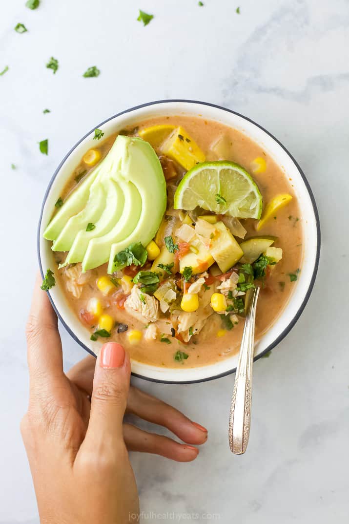 a hand holding a bowl of creamy crockpot chicken tortilla soup