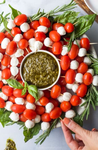 overhead photo of caprese skewers wreath with peso and a hand grabbing a skewer