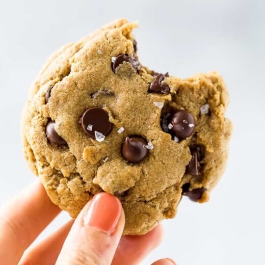 a hand holding a vegan pumpkin chocolate chip cookie with a bite taken out of it