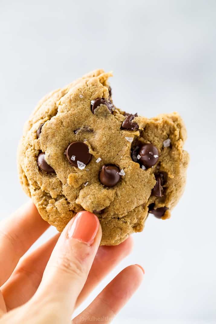 a hand holding a vegan pumpkin chocolate chip cookie with a bite taken out of it