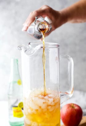 Pouring bourbon into pitcher with apple cider and ice.