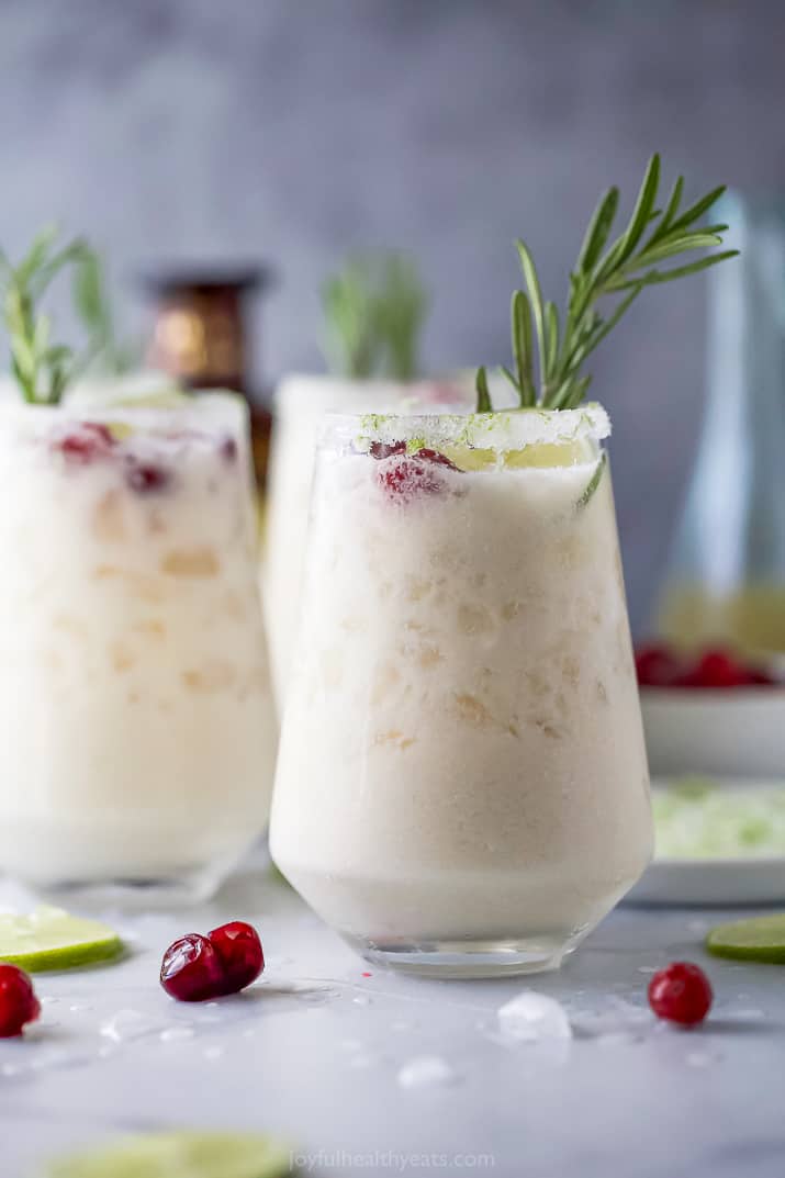 white christmas margarita recipe in a glass with cranberries and rosemary