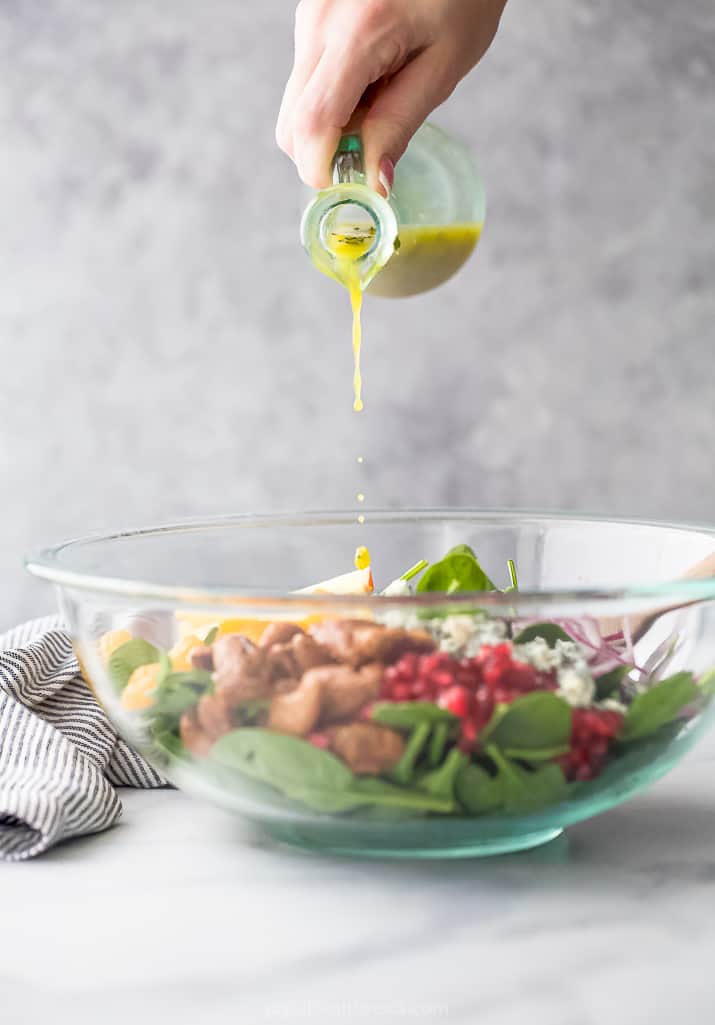 dressing being poured on the best spinach salad with apples